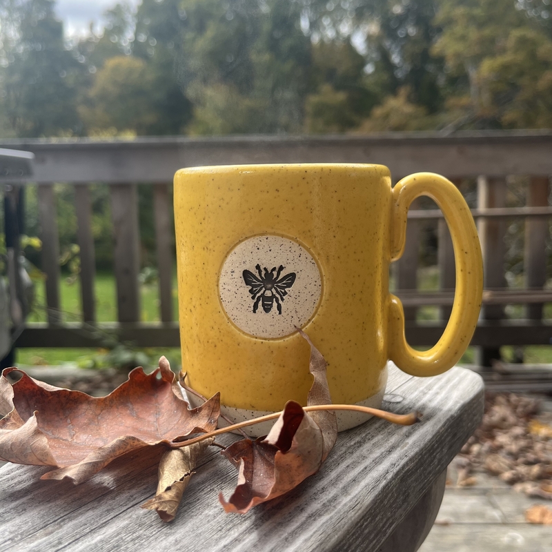 a yellow mug with a bee logo sitting outside