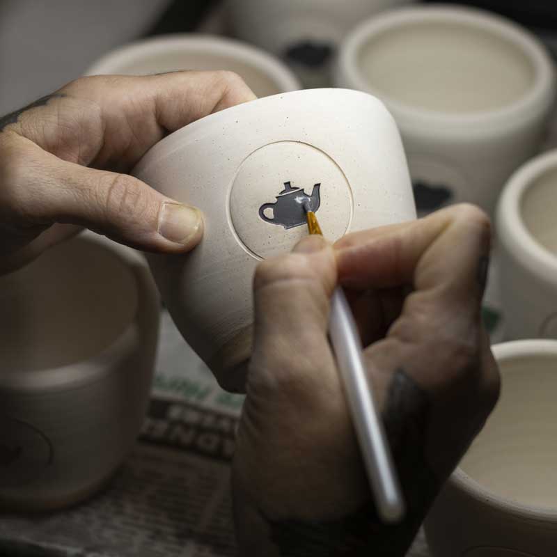 close-up of hands painting engobe onto a pottery mug